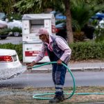 Senior man in work clothes watering grass on a street in İzmir, Türkiye with a hose.