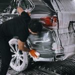 A person meticulously washing a car at a car wash using soap and a sponge.